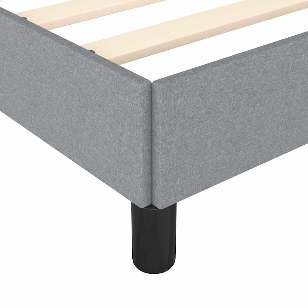 Closeup of a grey upholstered bed frame with black cylindrical legs and wooden slats visible