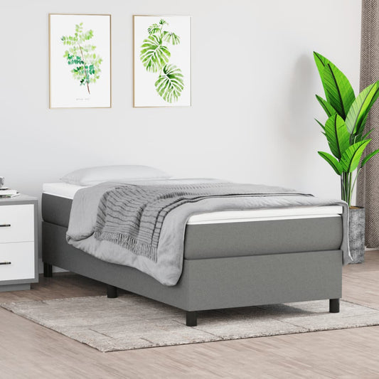Grey upholstered twin bed frame with a mattress and a folded blanket