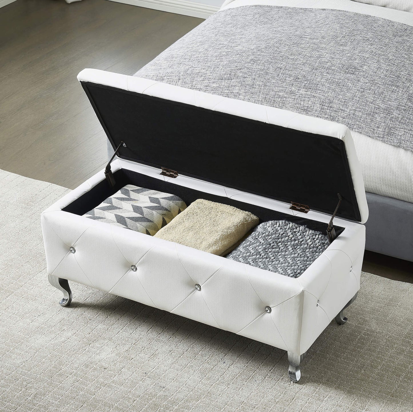 White tufted storage bench with crystal buttons and silver legs storing blankets