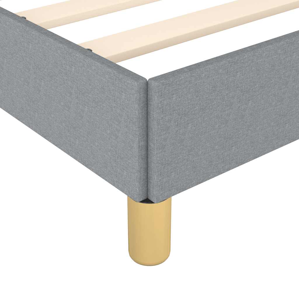 Closeup of a gray upholstered bed frame corner with golden metal legs and wooden slats visible