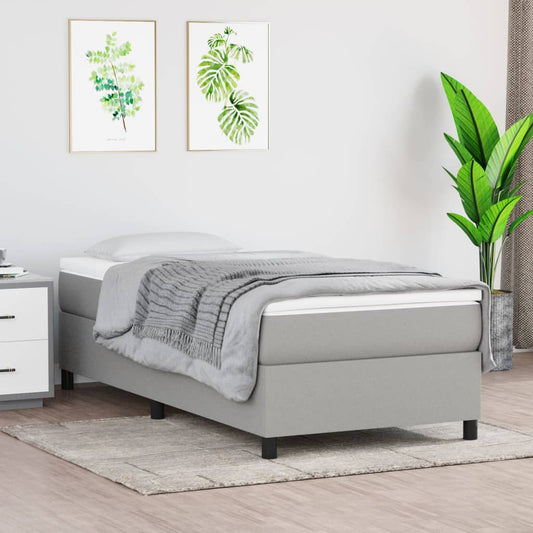 Grey upholstered twin bed frame with a white mattress and a gray throw blanket