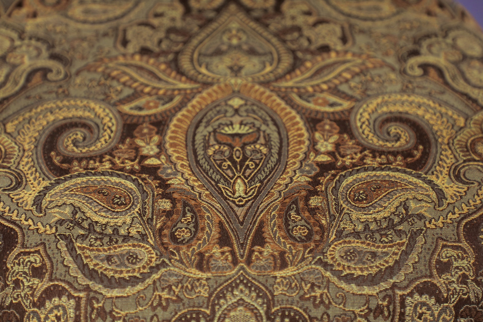 Detailed view of a tapestry fabric with a rich paisley pattern in gold and brown tones