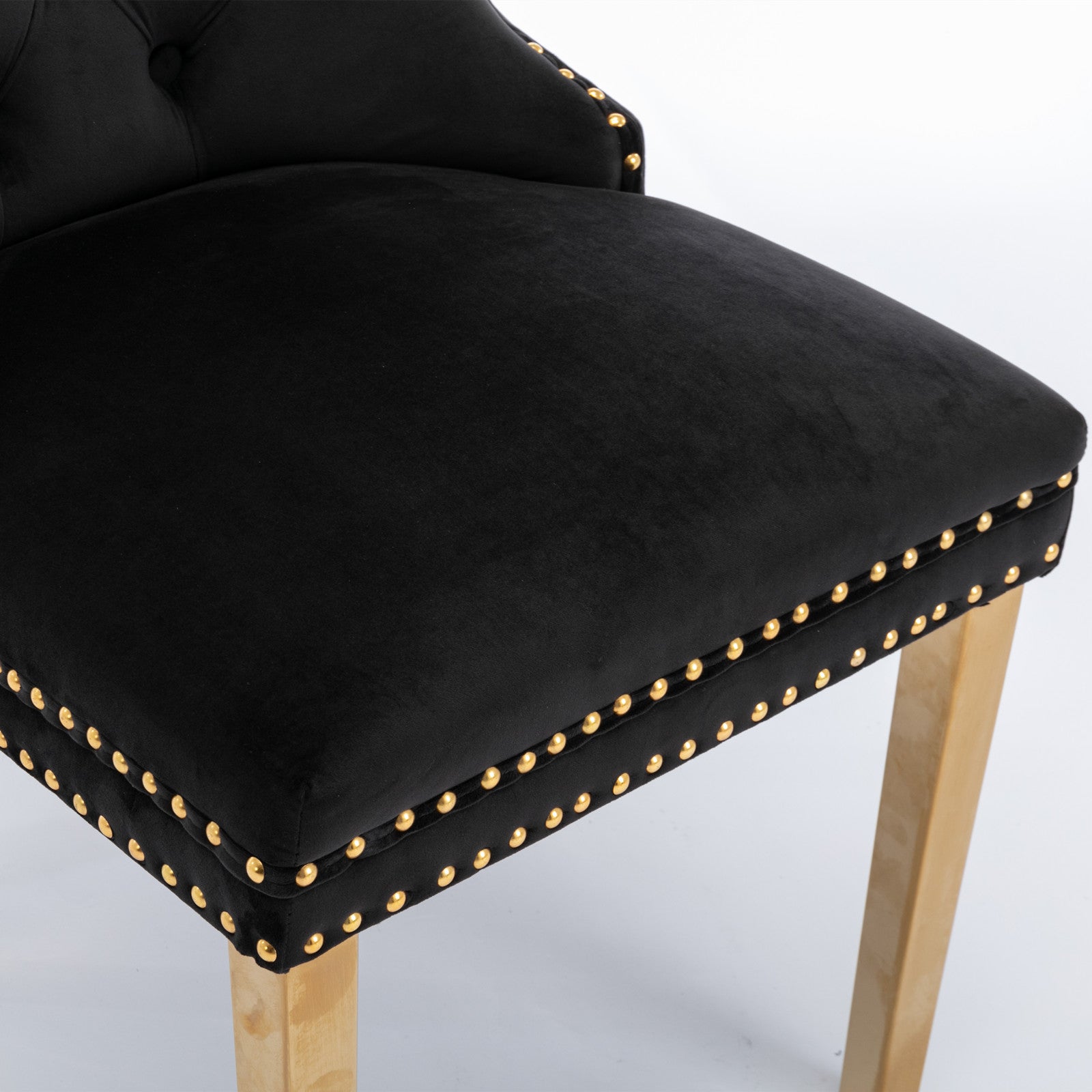 Closeup of a black velvet tufted bar stool with gold nailhead trim and a wooden leg