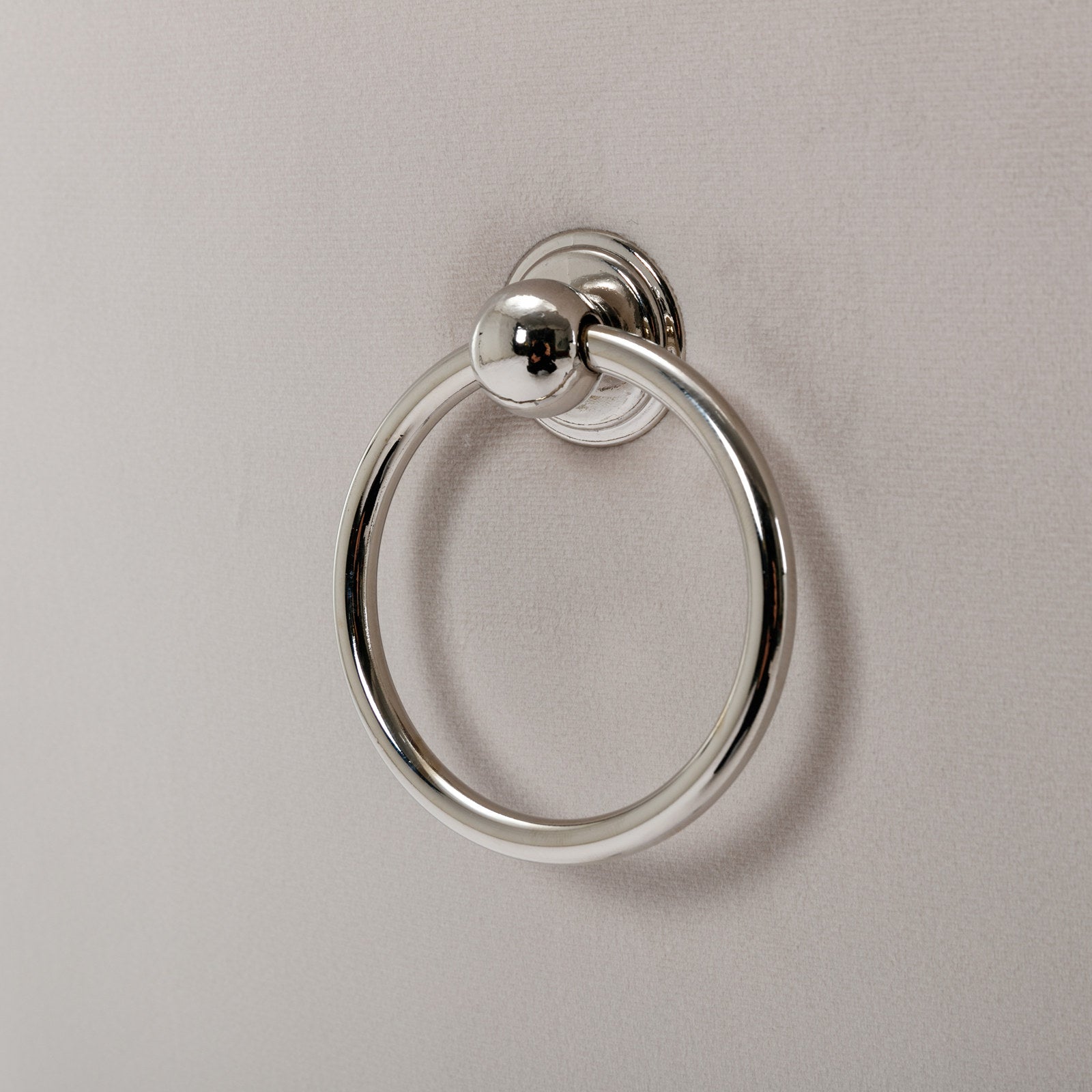 Polished chrome ring towel holder on a textured beige surface