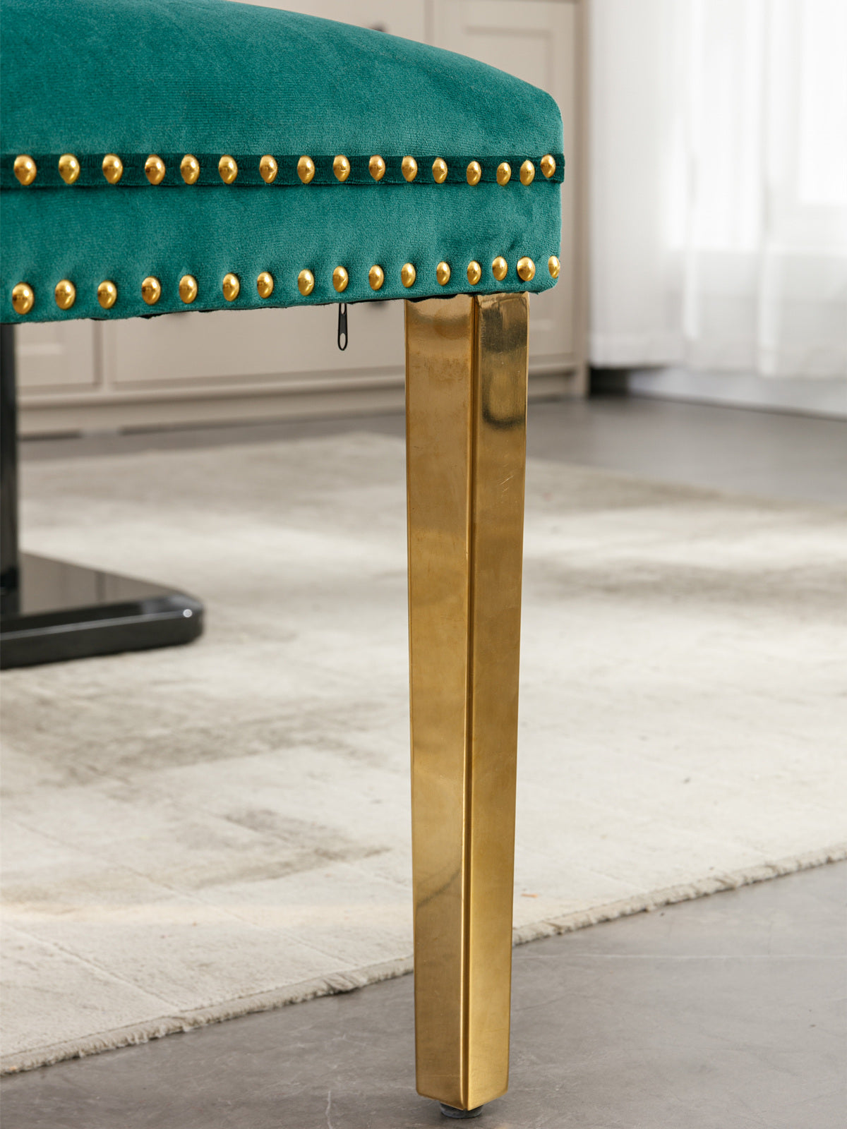 Emerald green velvet stool with gold studded trim and a sleek gold metal leg
