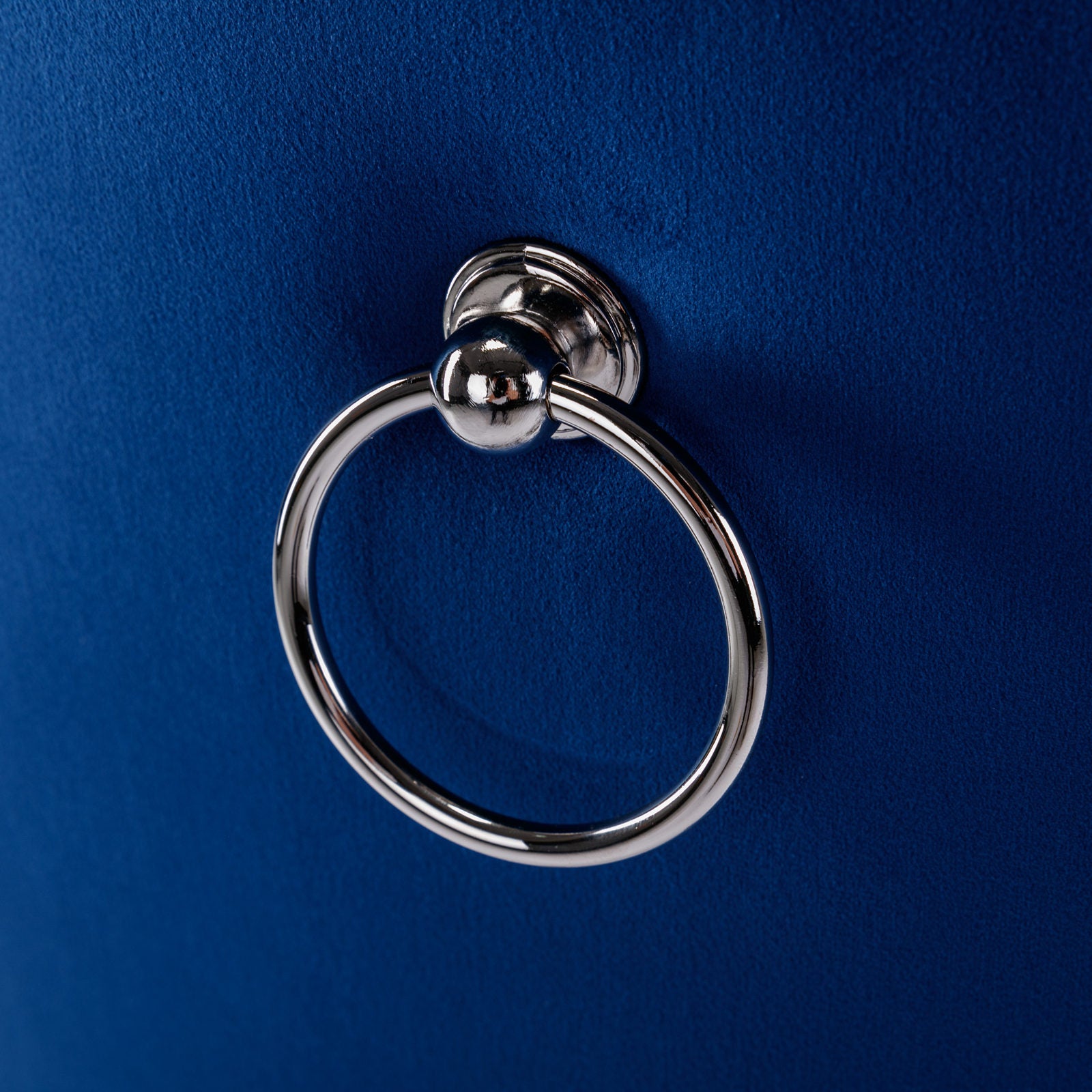 Closeup of a polished silver ring pull handle on a tufted royal blue velvet ottoman
