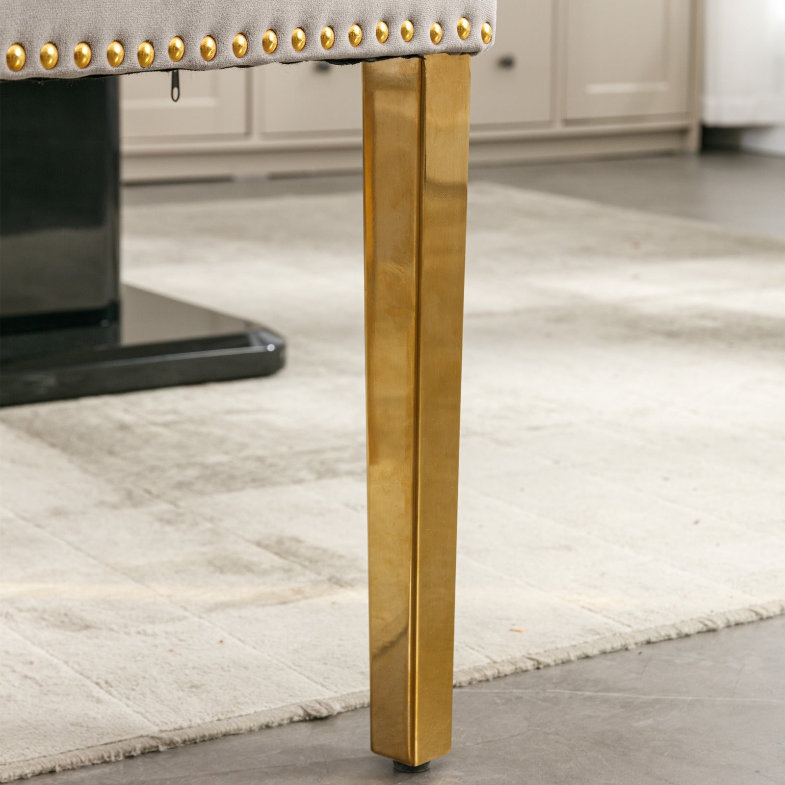 Gray upholstered bench with gold nailhead trim and a single gold metal leg
