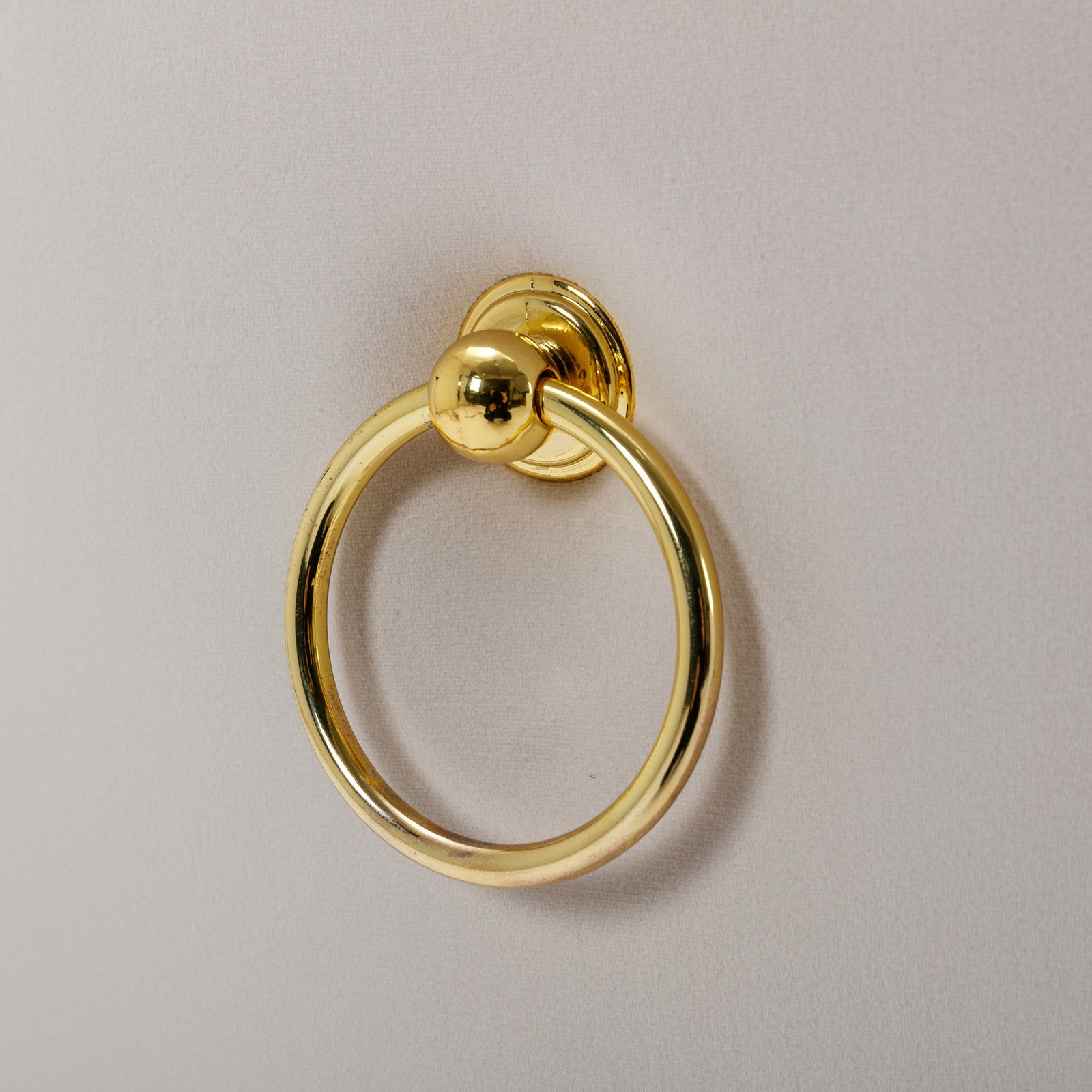Polished brass ring pull with round knob on light beige upholstery