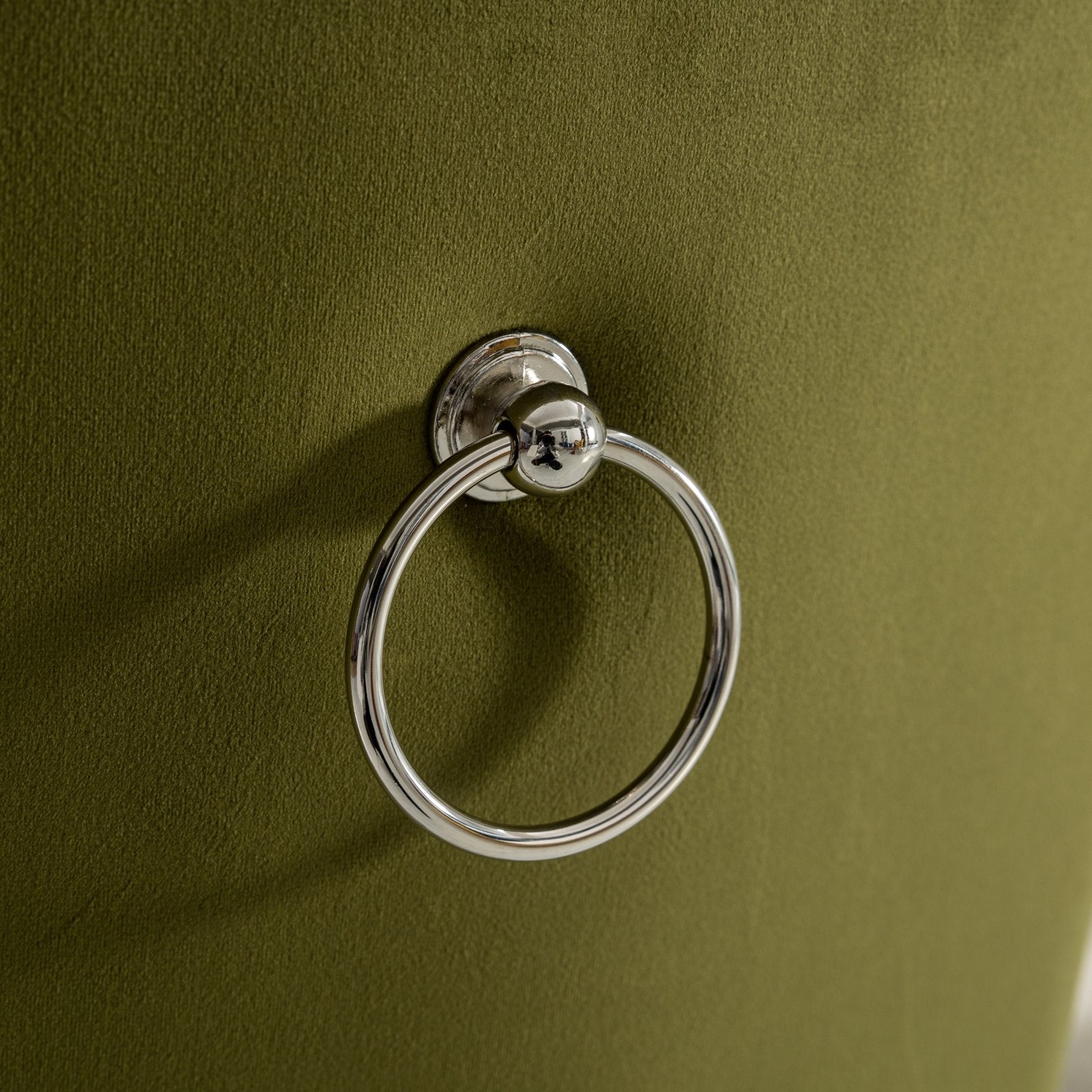 Closeup of a silver ring pull handle on olive green velvet upholstery