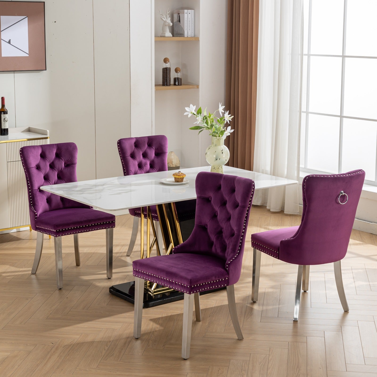 Four deep purple velvet dining chairs with silver nailhead trim surround a white marbletop table