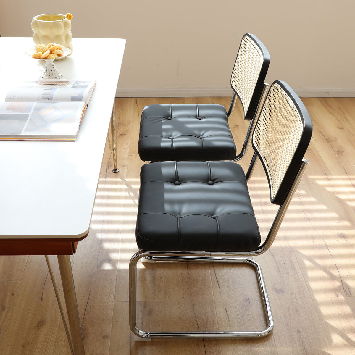 Two black faux leather dining chairs with cane backs and chrome frames