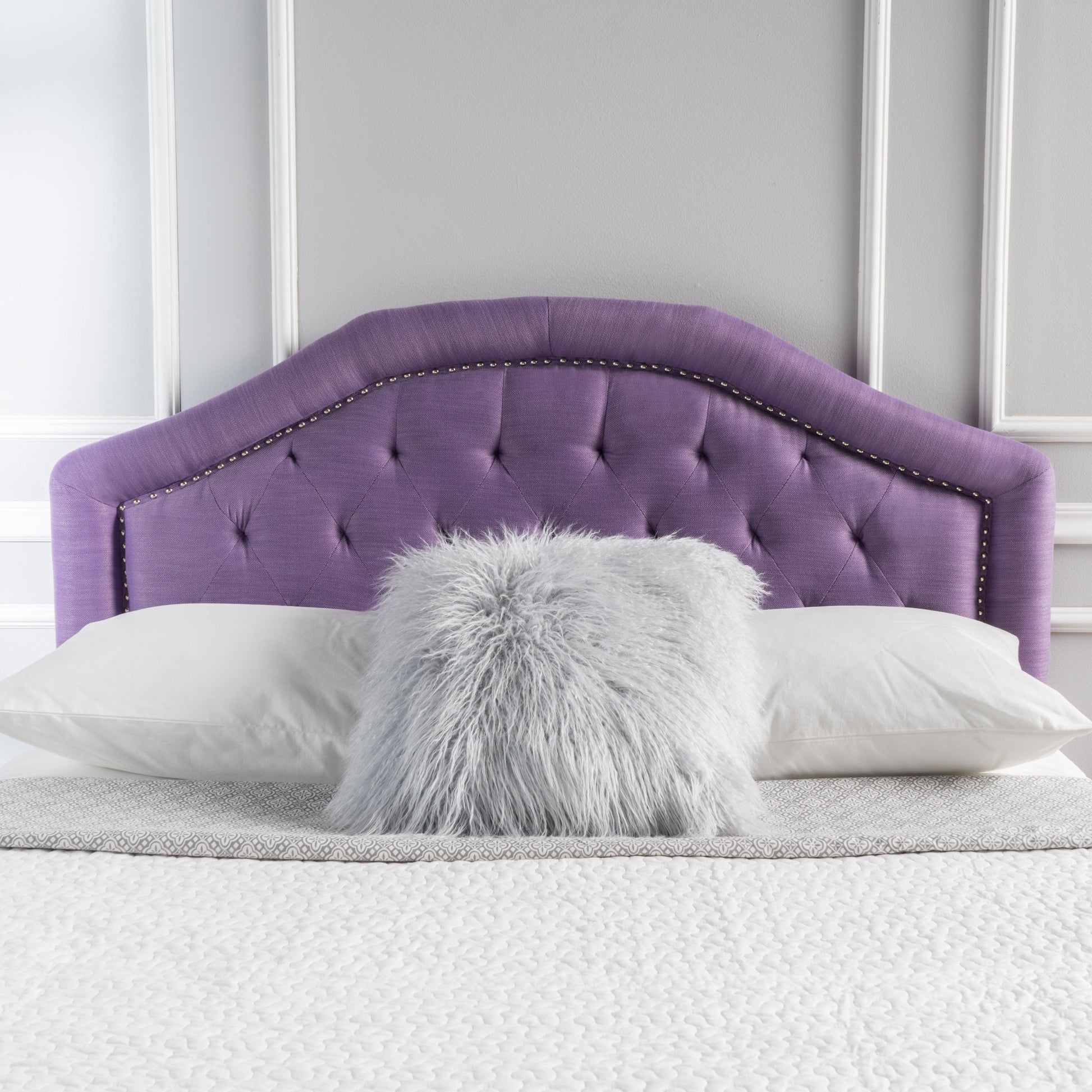 Tufted purple fabric headboard with nailhead trim on a bed with white pillows