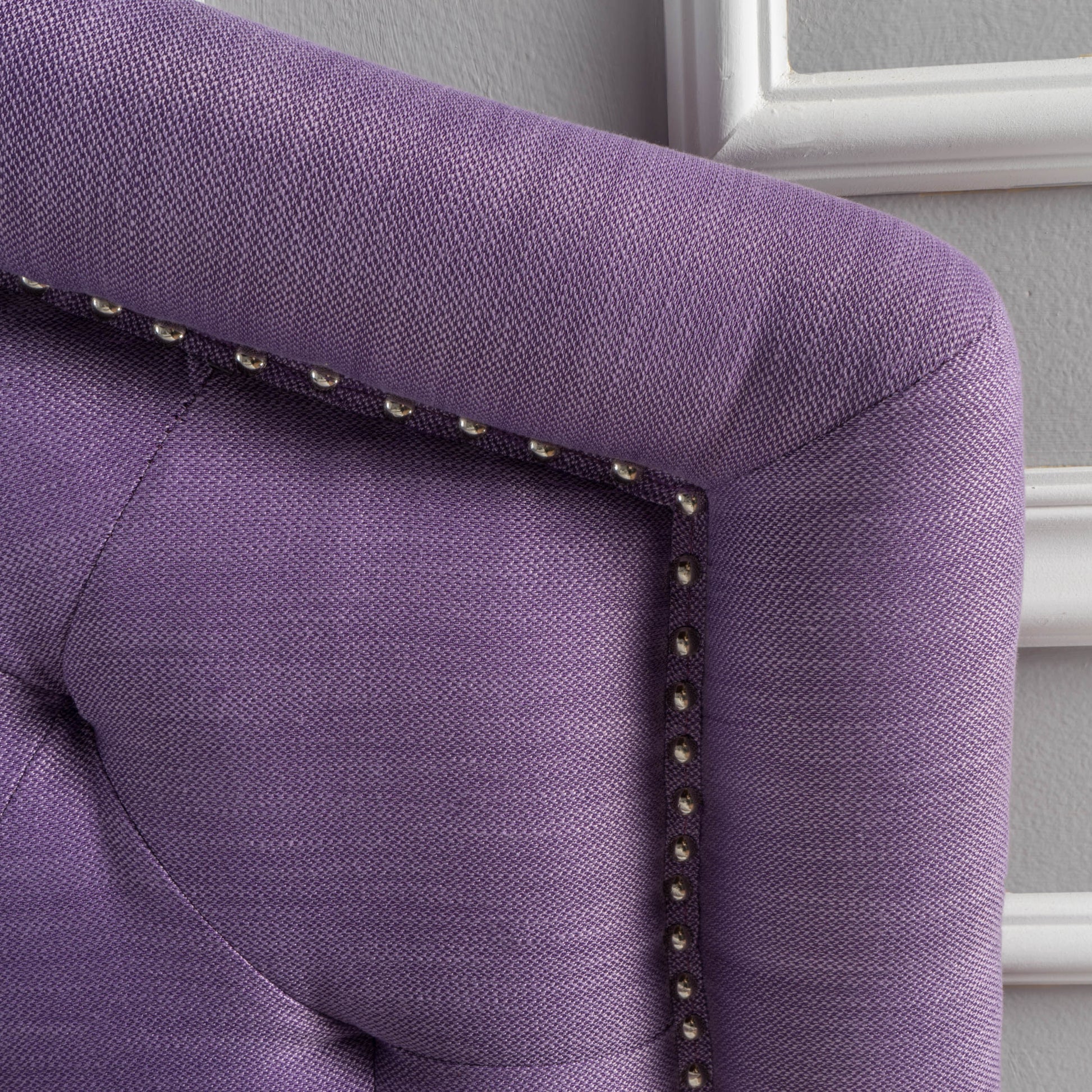 Closeup of tufted purple upholstered headboard with silver nailhead trim
