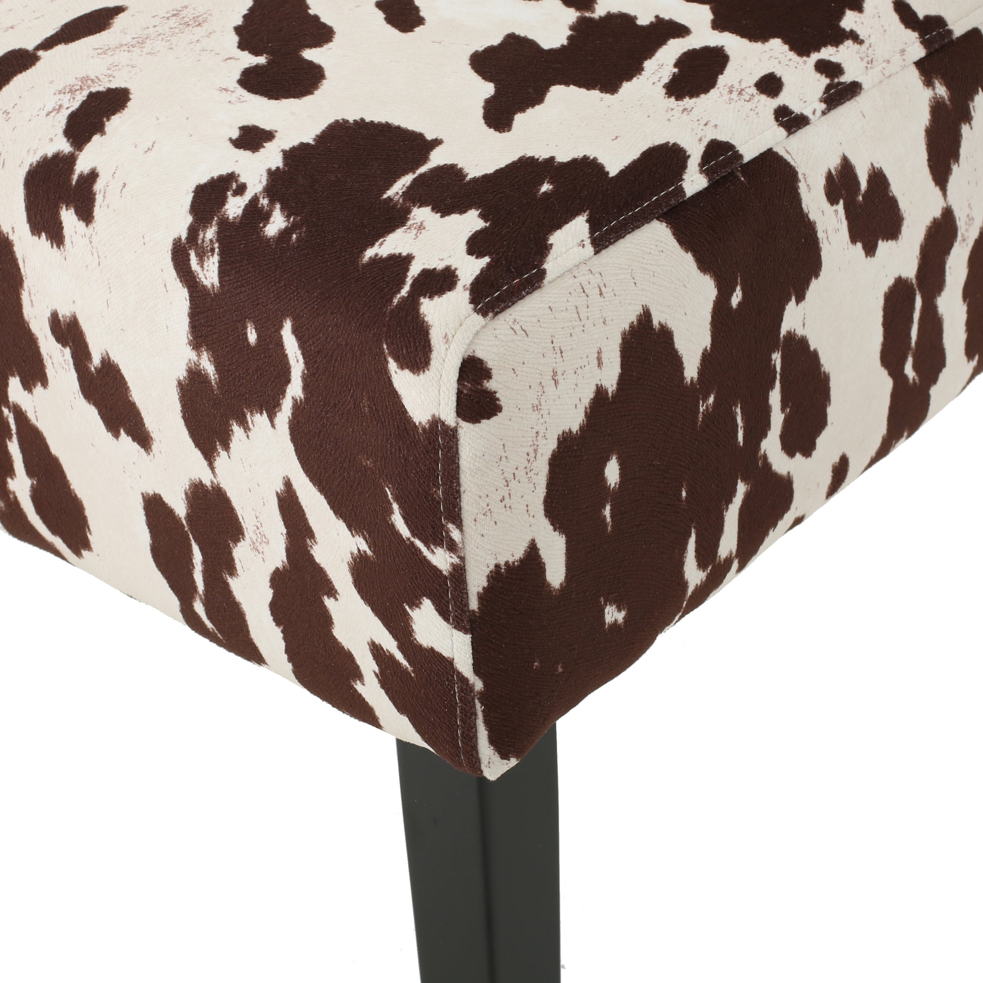 Brown and white cow print fabric on a chair seat edge with black leg