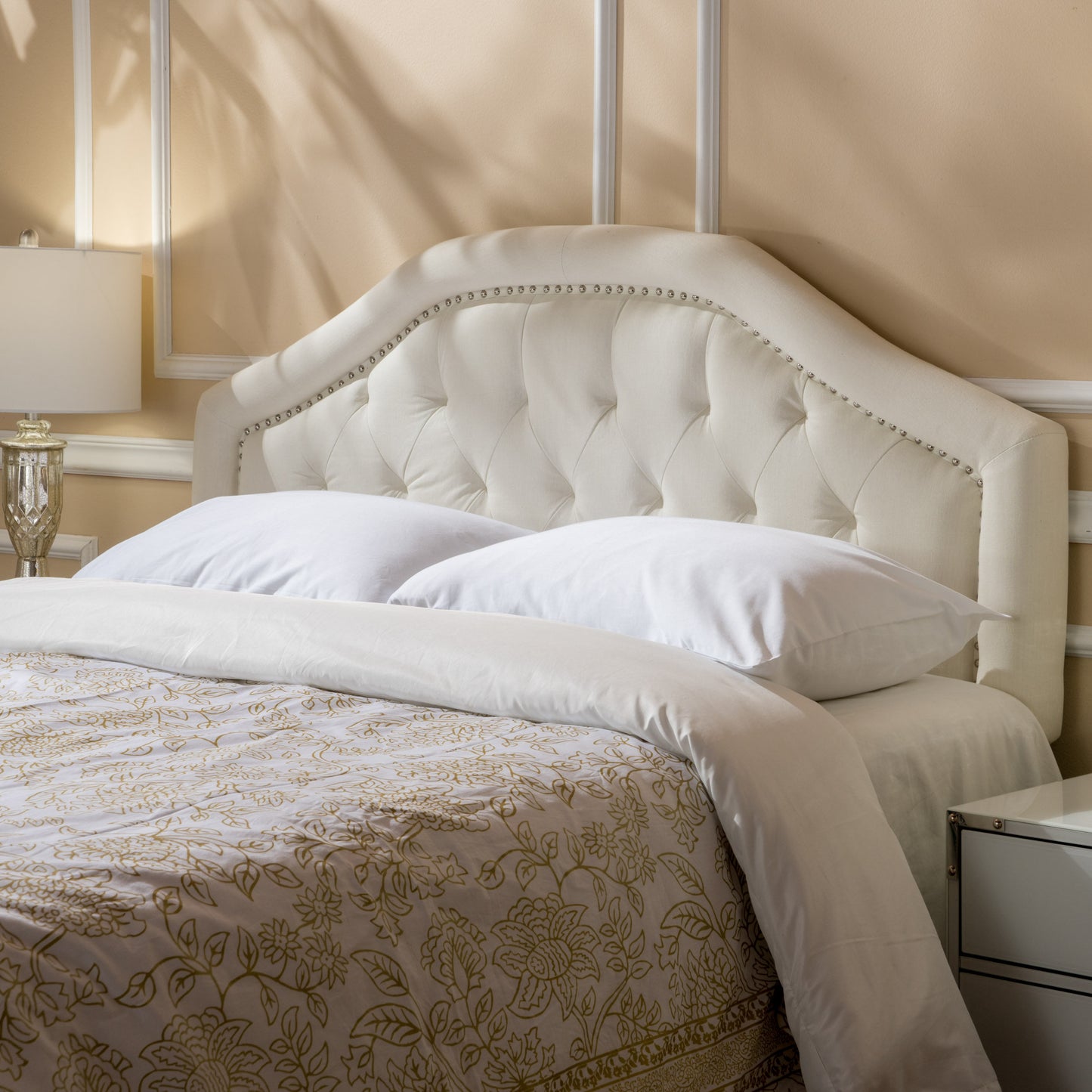 Cream upholstered tufted headboard with nailhead trim paired with white bedding for a luxurious bedroom set