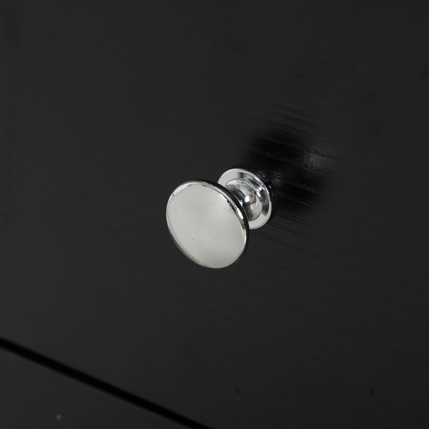 Round brushed nickel dresser knob on a black wooden surface