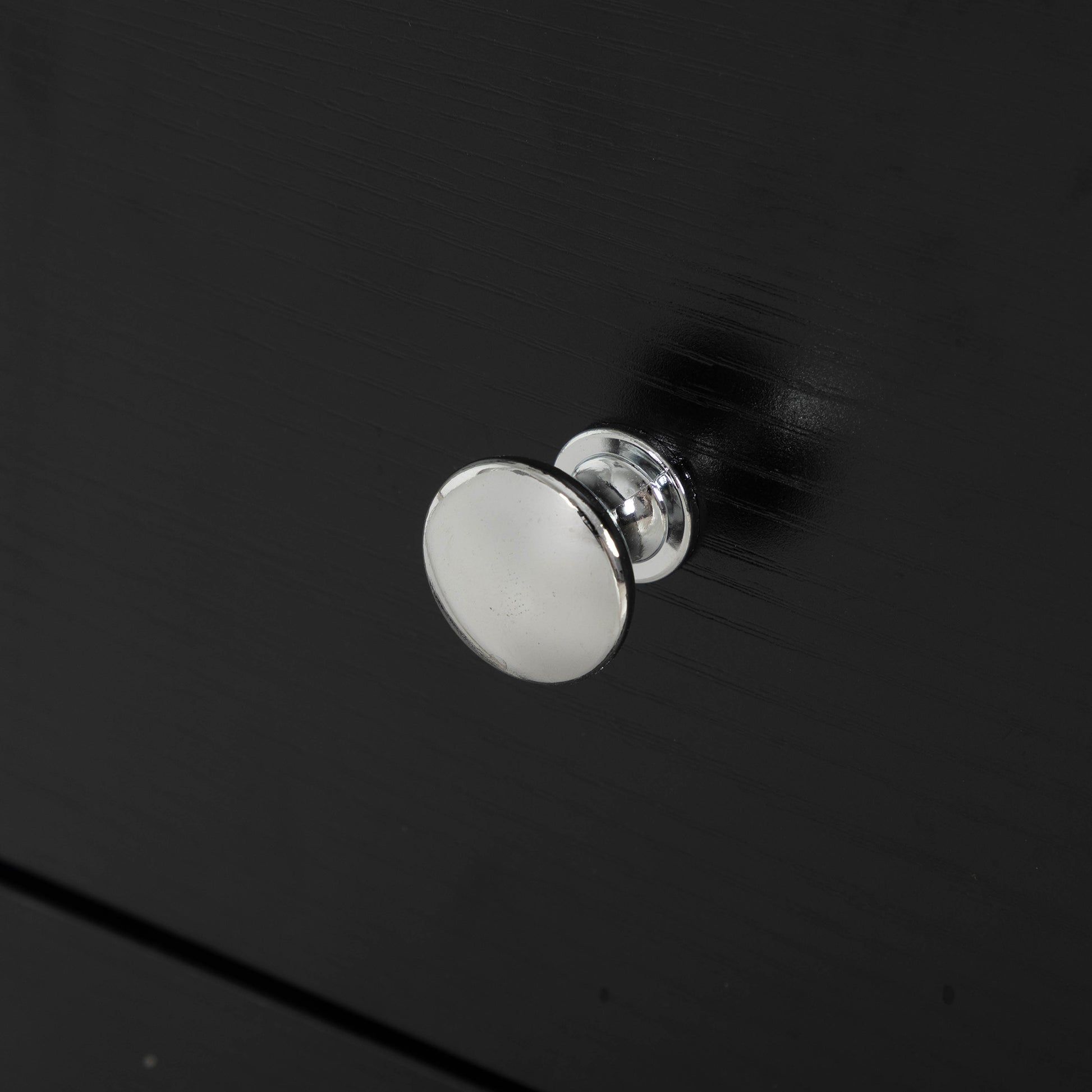 Round brushed nickel dresser knob on a black wooden surface