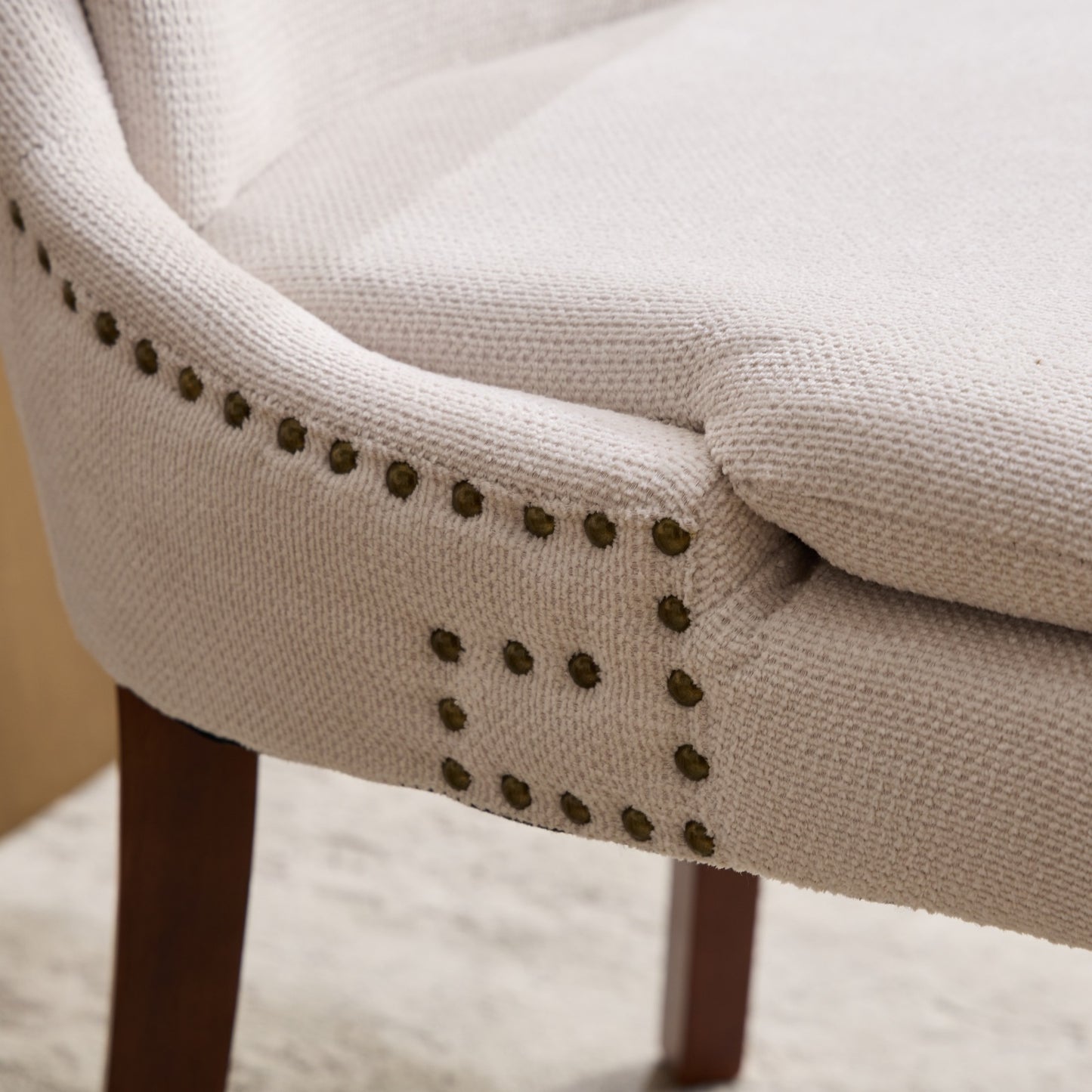 Cream upholstered accent chair with antique brass nailhead trim details and dark wood legs