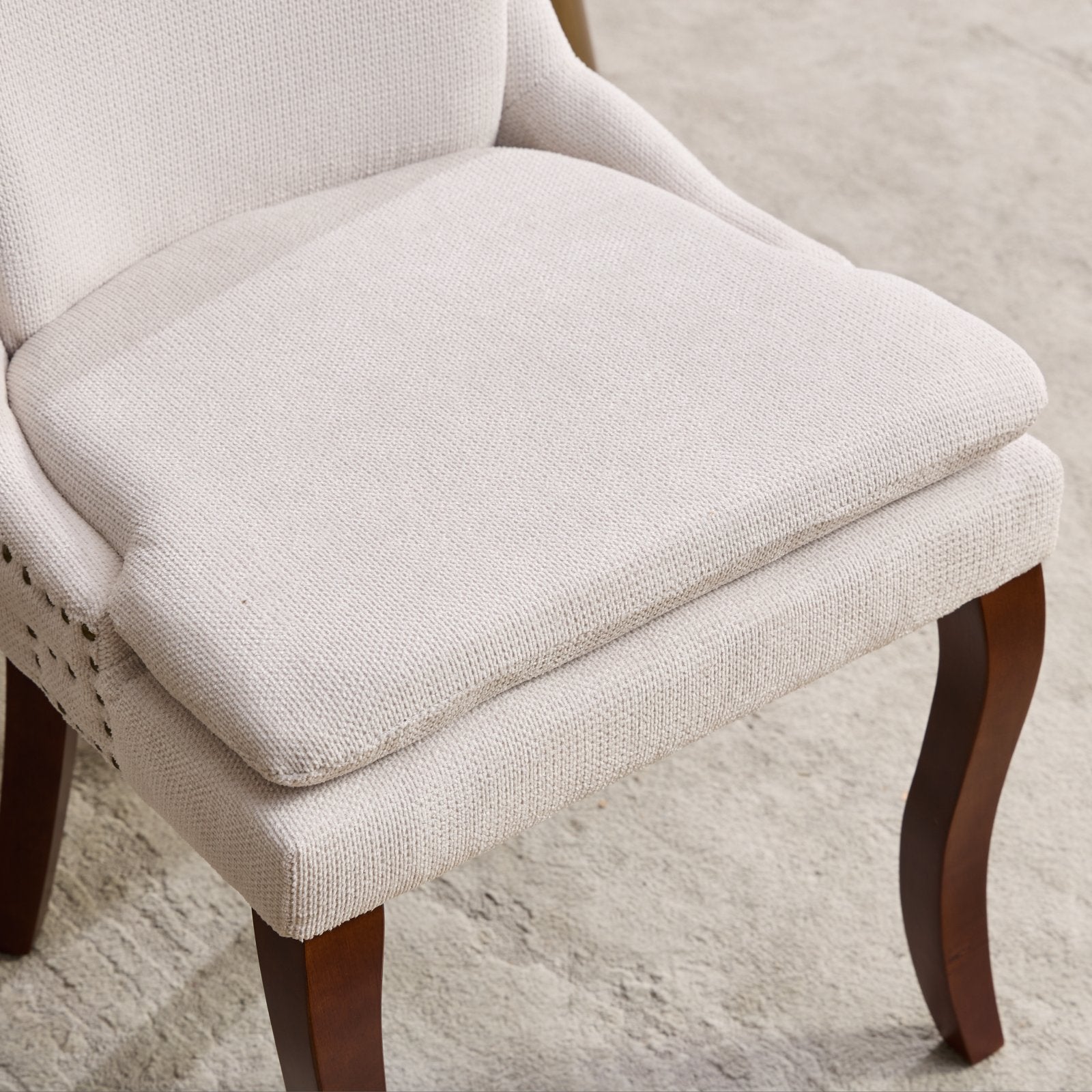 Cream upholstered dining chair with dark wood legs and subtle nailhead trim accent