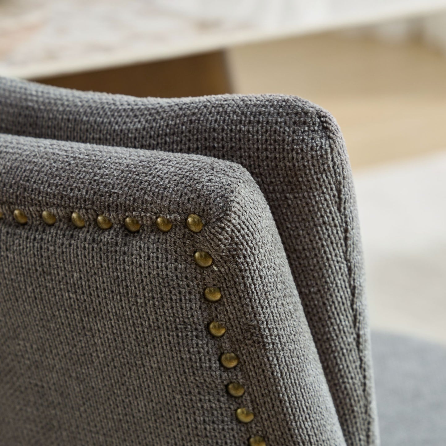 Closeup of a grey textured fabric armchair armrest with brass nailhead trim