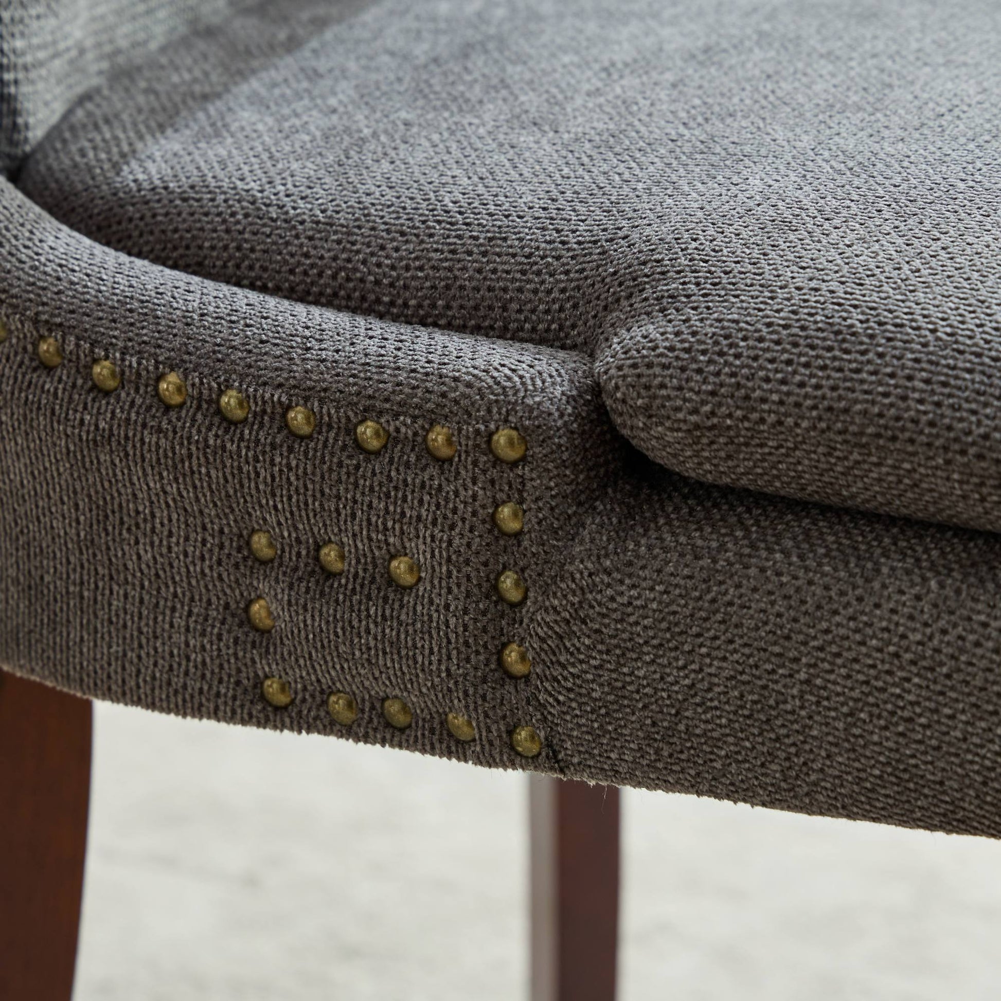 Dark gray upholstered chair detail with brass nailhead trim