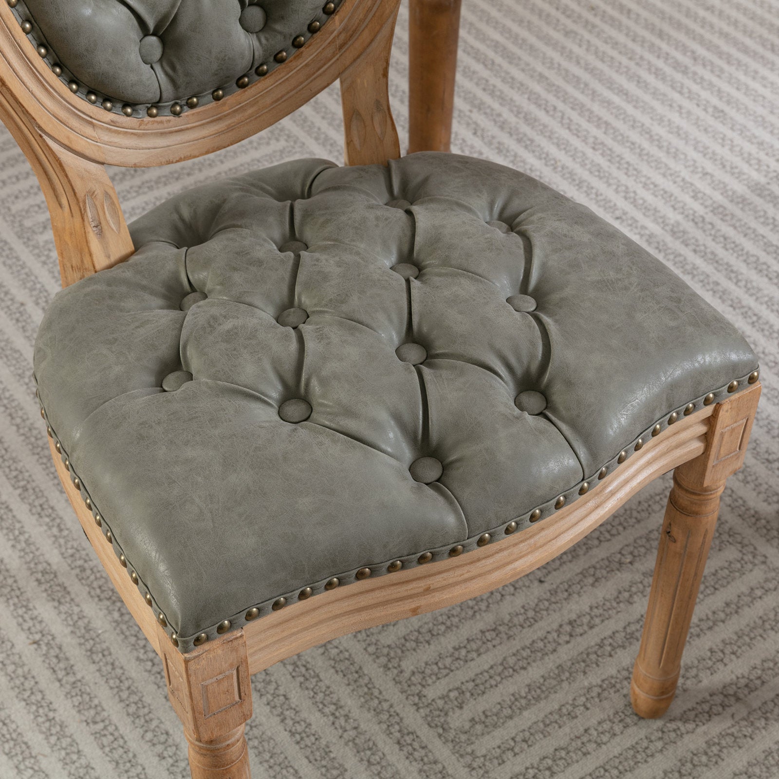 Tufted grey leather dining chair with antique brass nailhead trim and carved wooden frame