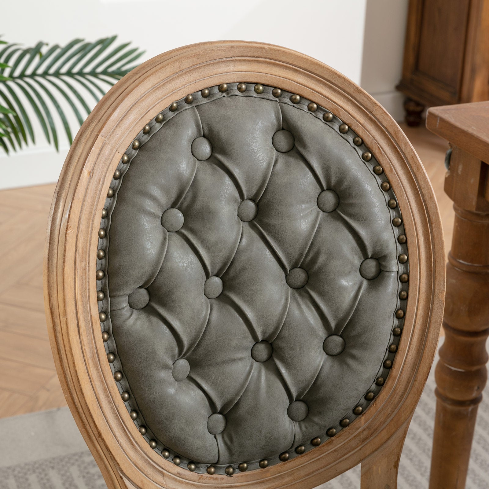Tufted grey faux leather oval back dining chair with distressed wood frame and brass nailhead trim