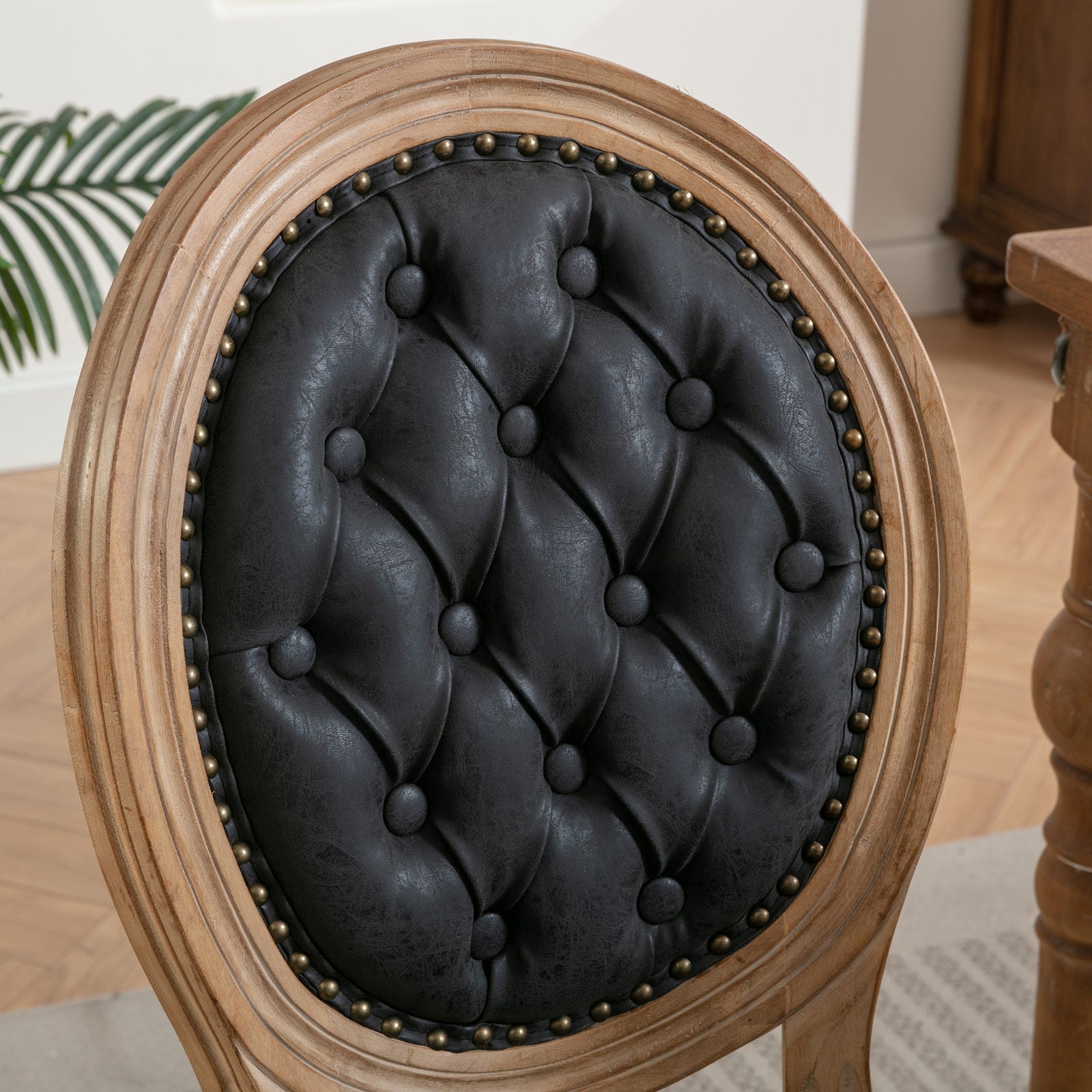 Tufted black faux leather dining chair back with antique brass nailhead trim and distressed wood frame