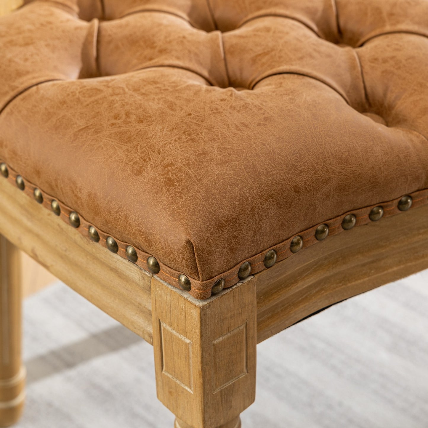 Tufted brown faux leather ottoman with antique brass nailhead trim and distressed wood legs