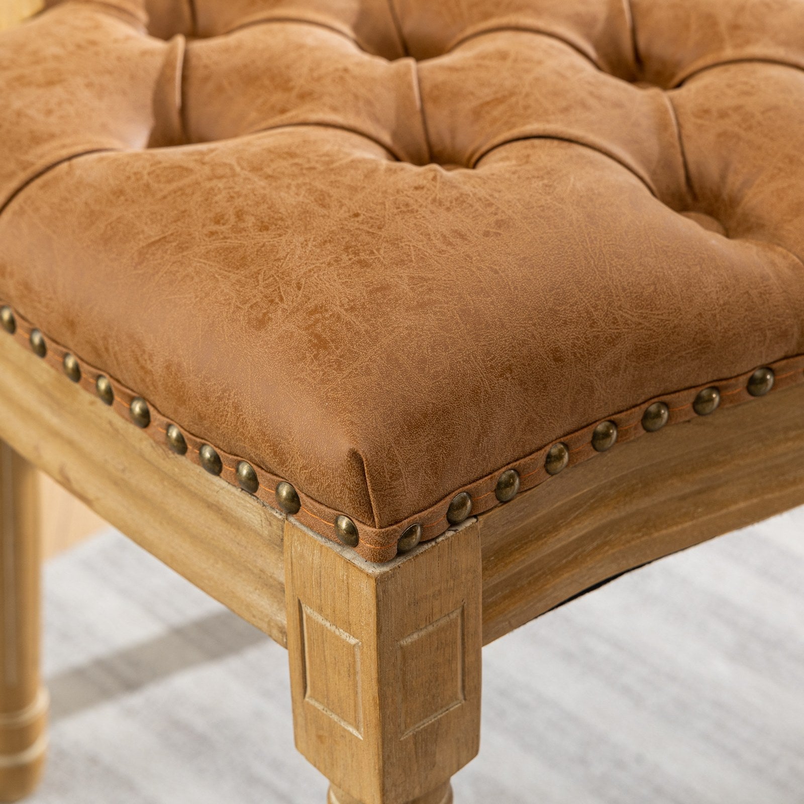 Tufted brown faux leather ottoman with antique brass nailhead trim and distressed wood legs
