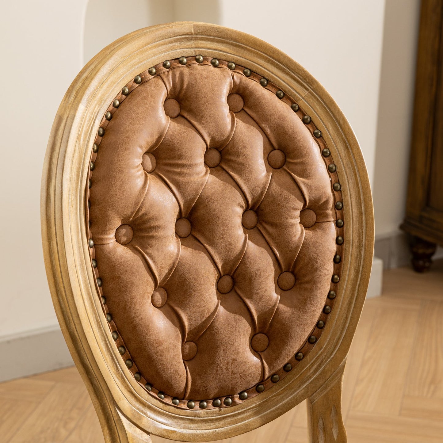 Tufted cognac leather armchair backrest with ornate antique brass nailhead trim and distressed wood frame