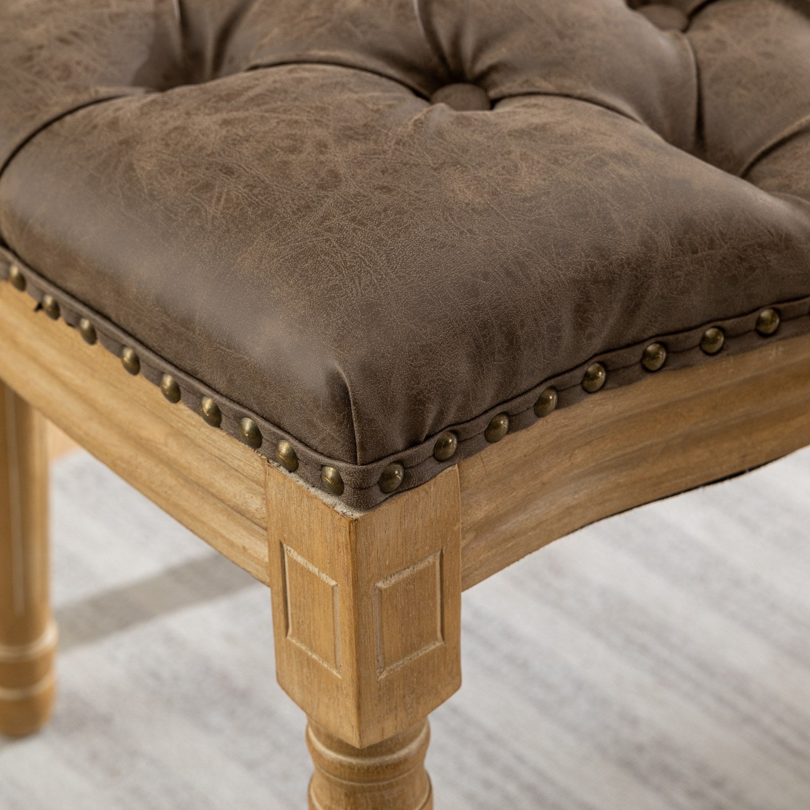 Tufted brown faux leather ottoman with antique brass nailhead trim and distressed wood legs