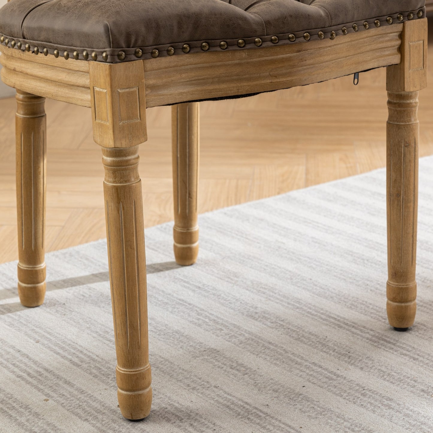 Tufted brown faux leather vanity stool with nailhead trim and carved wood legs