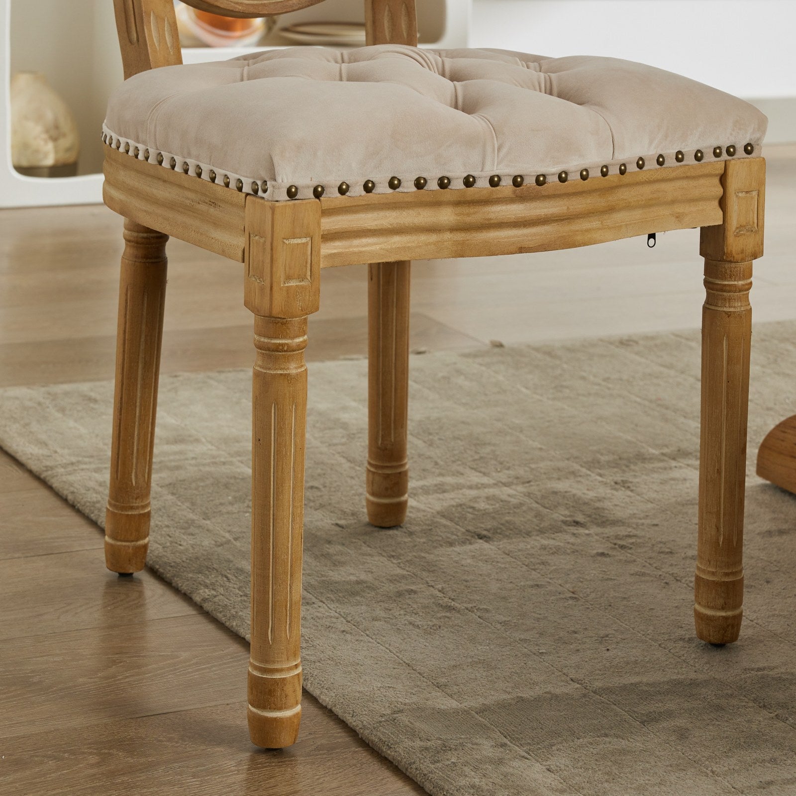 Tufted beige velvet dining chair with antique brass nailhead trim and carved wooden legs