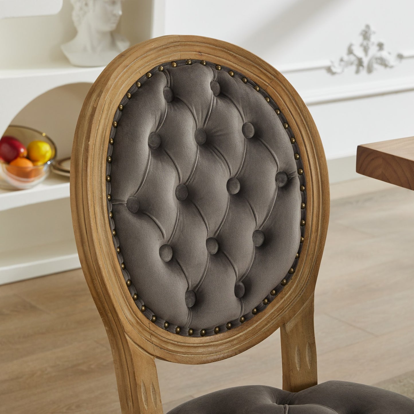 Tufted grey velvet oval chair back with ornate nailhead trim and distressed wood frame