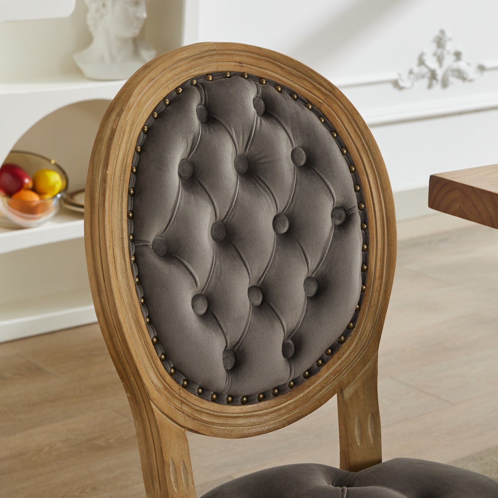 Tufted grey velvet oval chair back with ornate nailhead trim and distressed wood frame