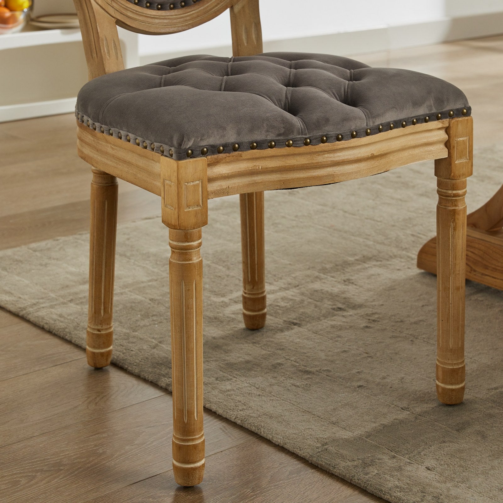 Tufted grey velvet dining chair with carved wooden frame and brass nailhead trim