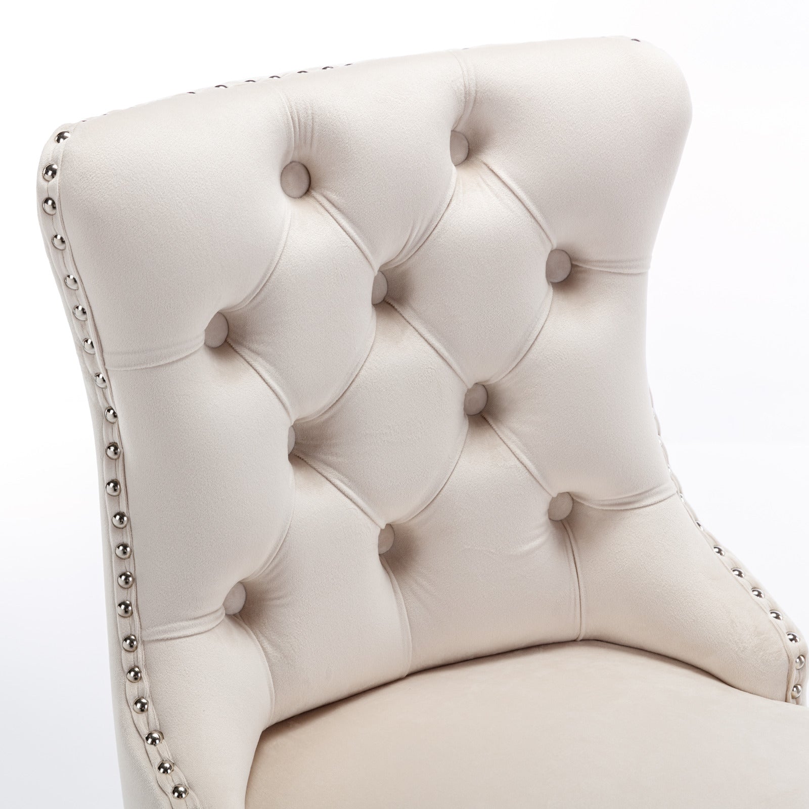 Closeup of a tufted cream velvet dining chair with silver nailhead trim
