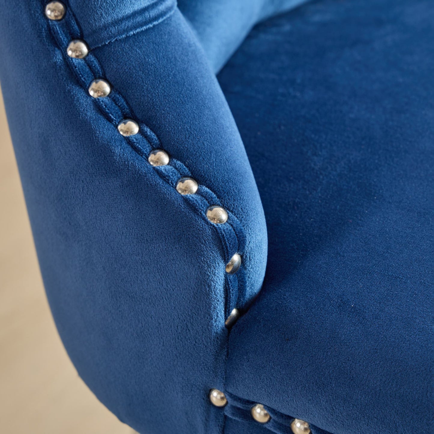 Closeup of plush navy blue velvet armchair armrest with silver nailhead trim detailing