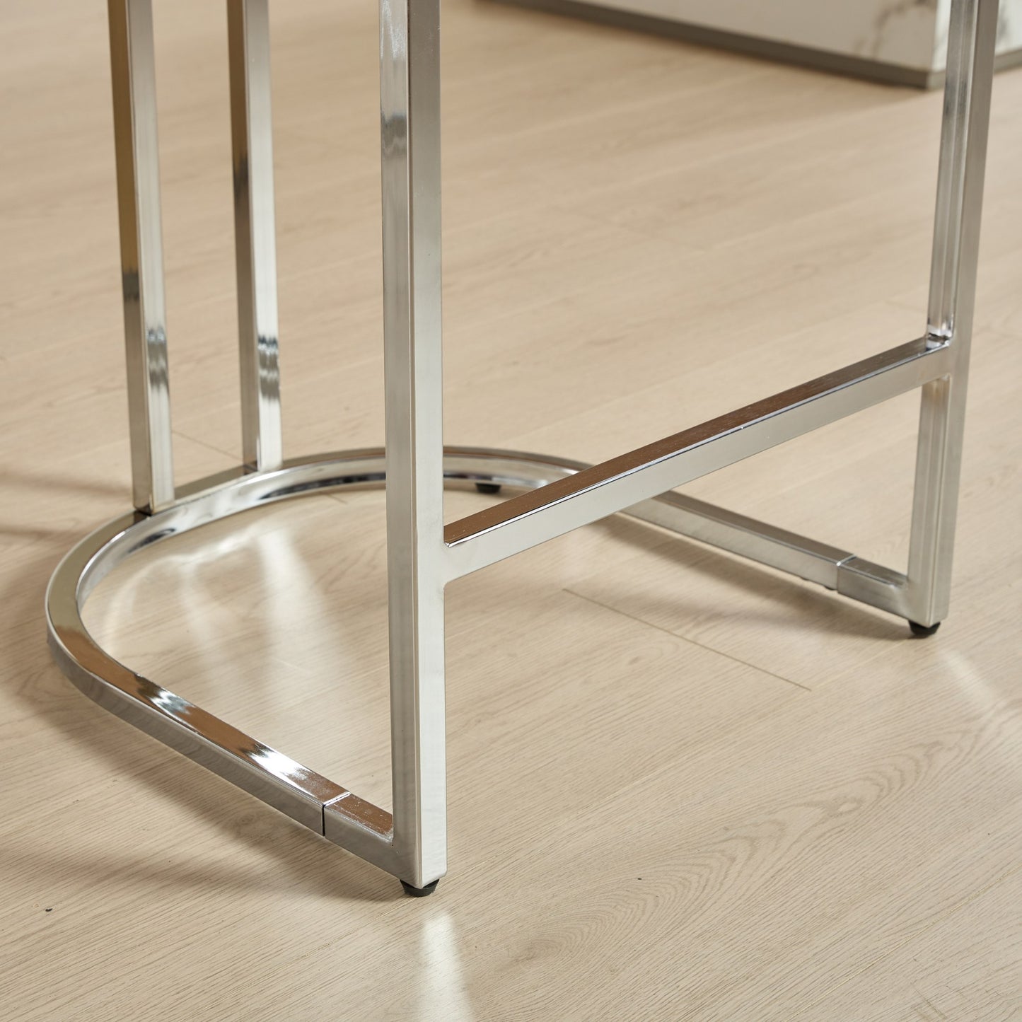Polished chrome bar stool base with a rounded footrest and square legs on a wood floor