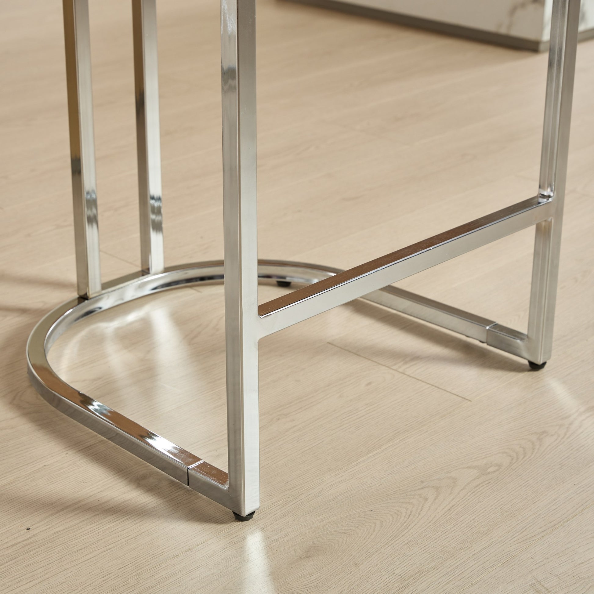 Polished chrome bar stool base with a rounded footrest and square legs on a wood floor