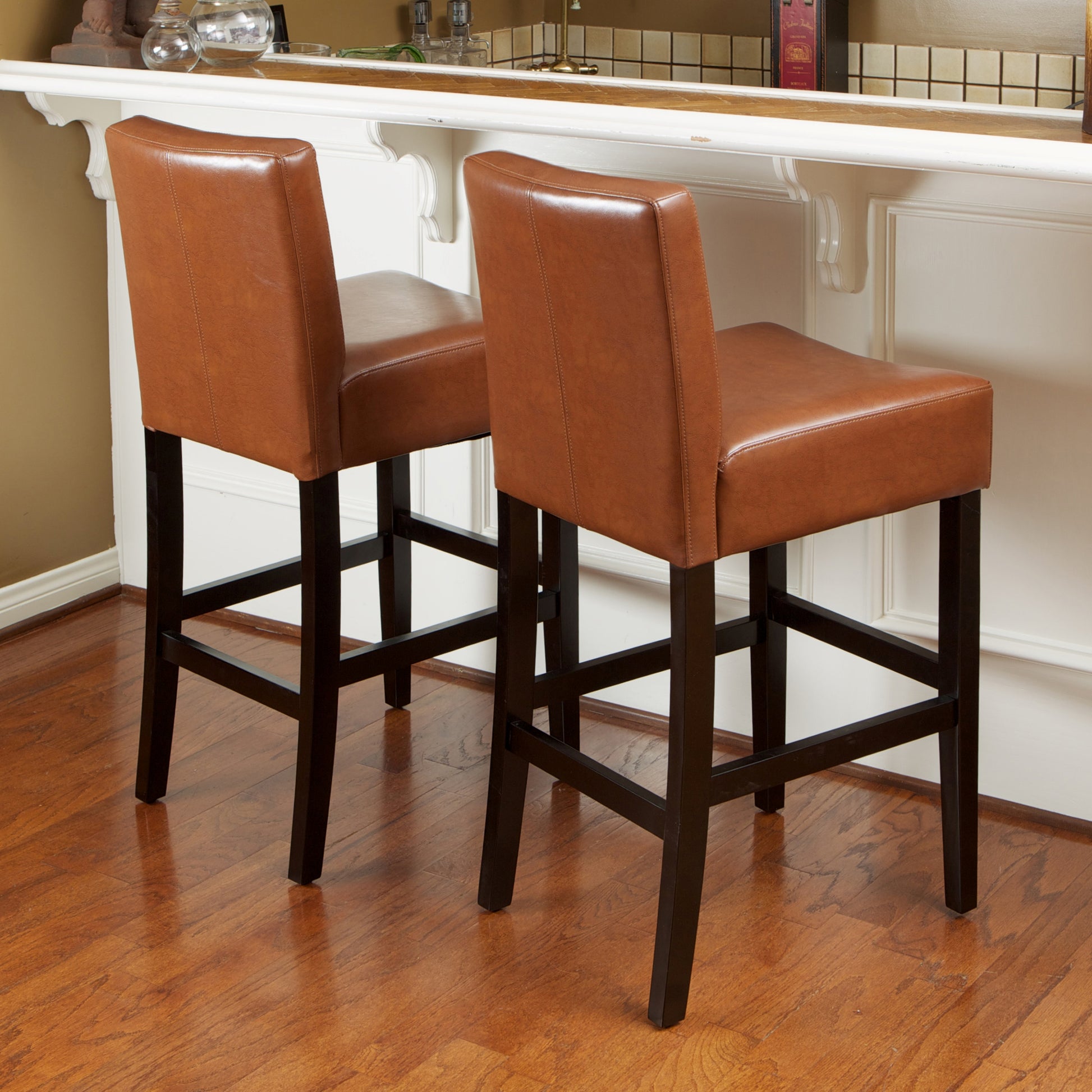 Two brown faux leather bar stools with dark wood frames on a hardwood floor