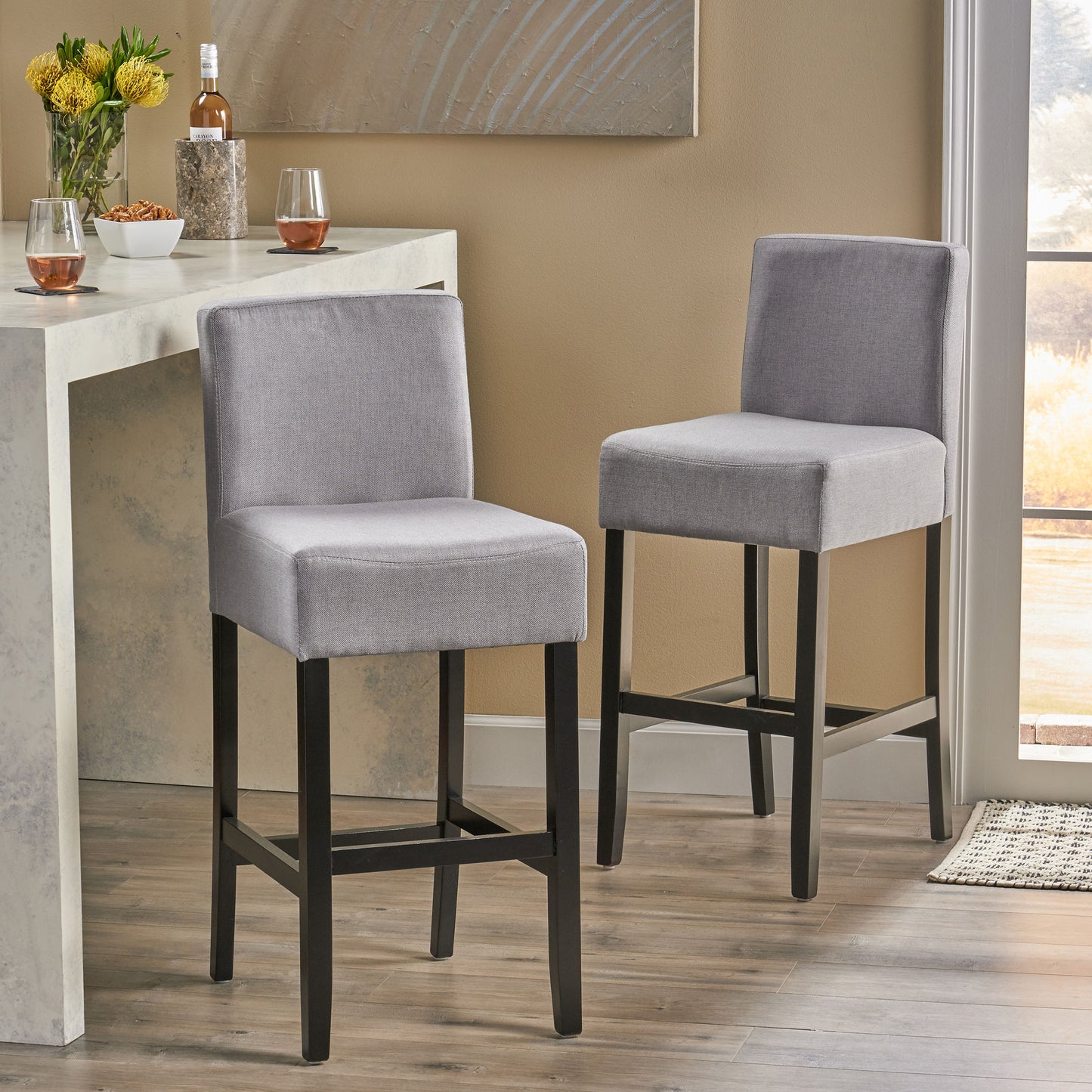 Two grey upholstered bar stools with dark wood legs in a modern kitchen setting