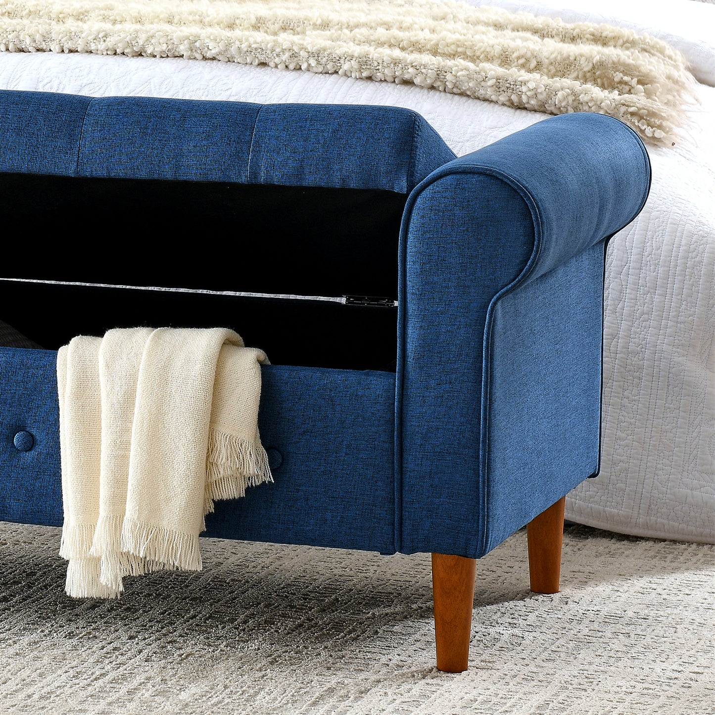 Tufted navy blue storage bench with rolled arms and a folded cream throw