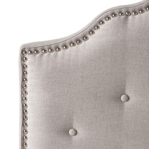 Tufted light gray fabric headboard detail with silver nailhead trim