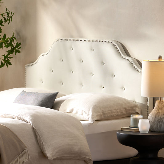 Tufted cream upholstered headboard with silver nailhead trim on a bed