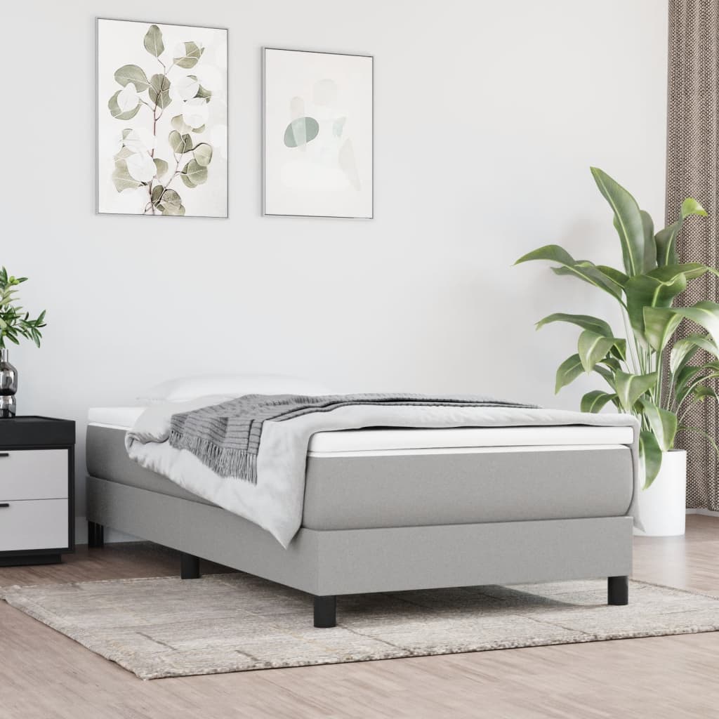 Gray upholstered single bed frame with white mattress and a folded grey blanket