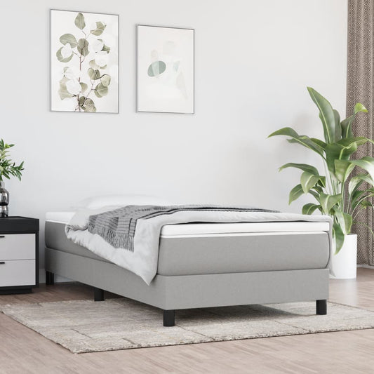 Gray upholstered single bed frame with white mattress and a folded grey blanket