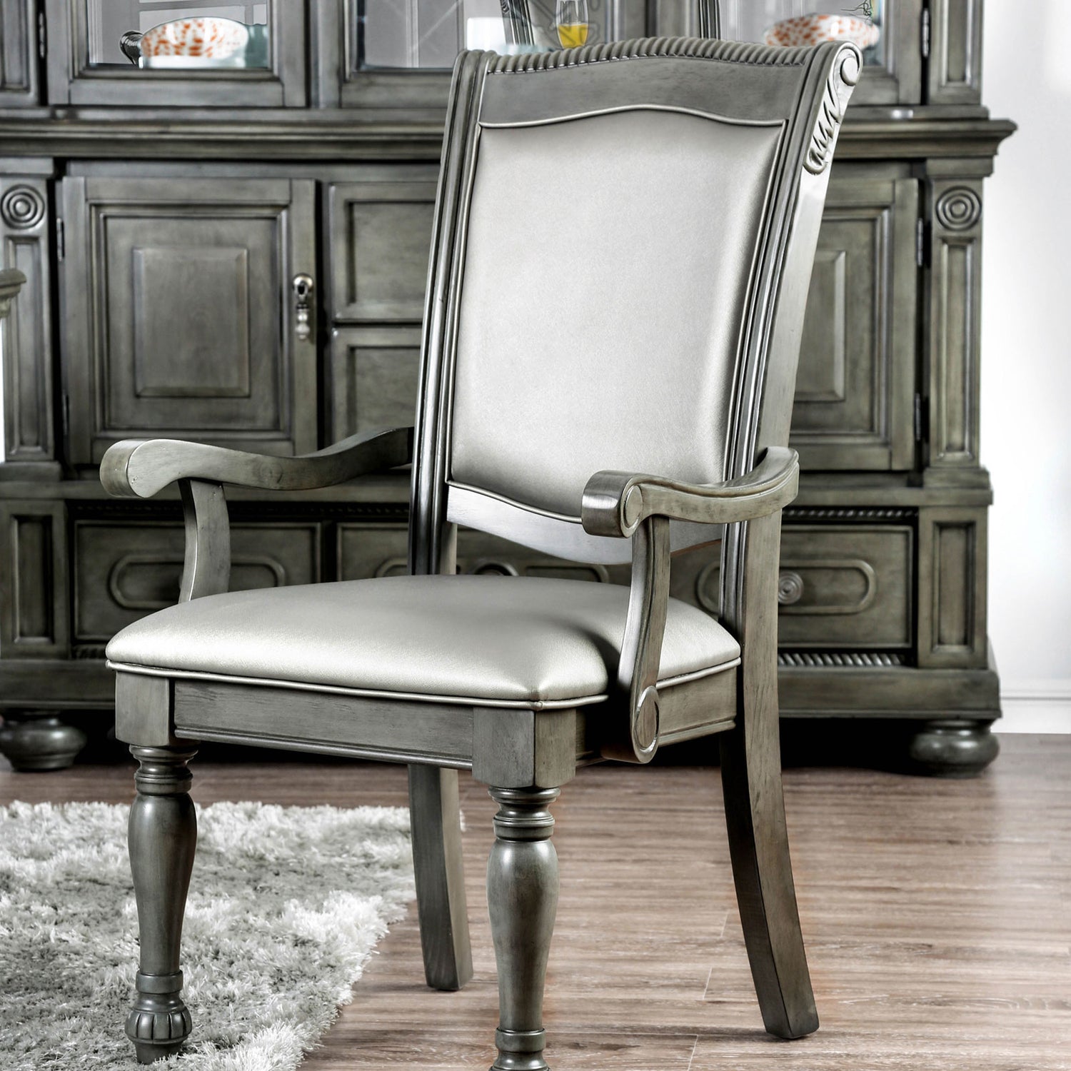 Grey upholstered arm chair with carved wood details and matching hutch