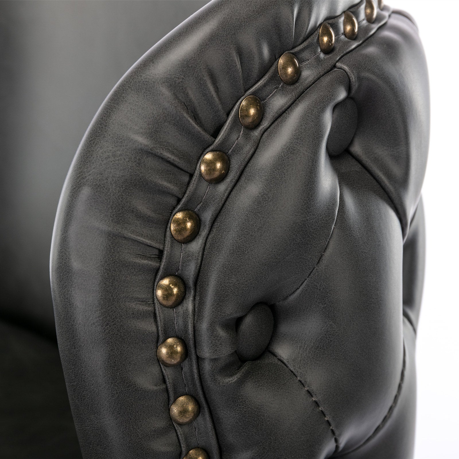 Dark gray faux leather armchair detail with brass nailhead trim and tufted accents